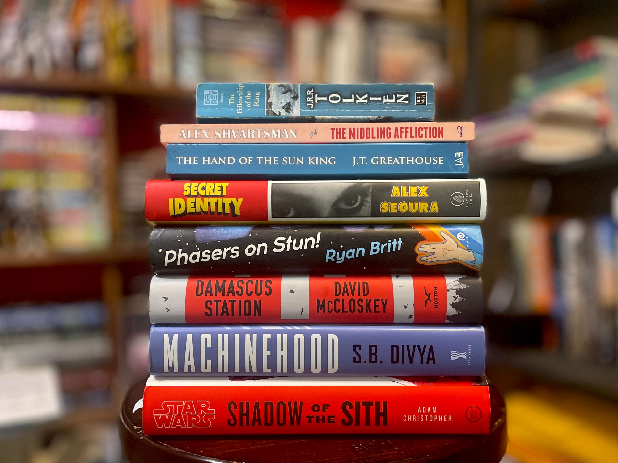 A stack of books: Fellowship of the Ring, The MIddling Affliction, The Hand of the Sun King, Secret Identity, Phasers on Stun! Damascus Station, Machinehood, and Shadow of the Sith