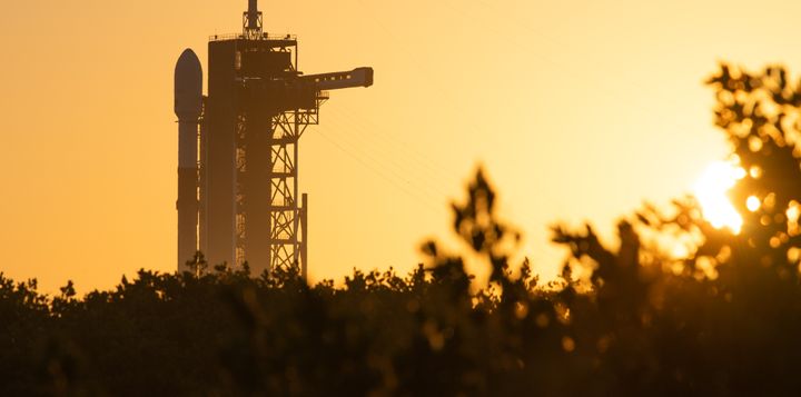 A Falcon-9 rocket sits at the launch tower against a golden-yellow sky.