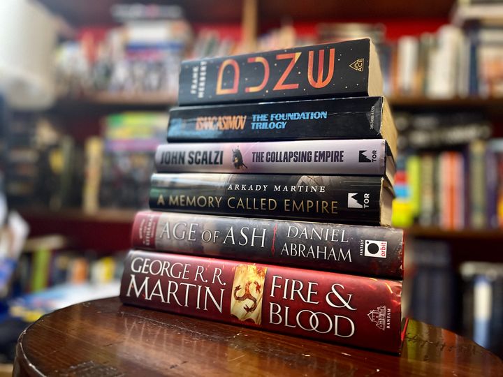 A stack of books: Dune, Foundation, The Collapsing Empire, A Memory Called Empire, Age of Ash, and Fire & Blood