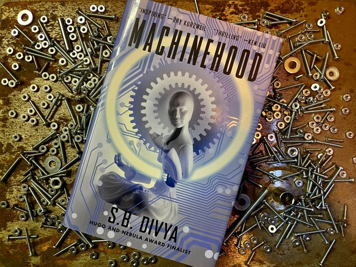 A picture of S.B. Divya’s novel Machinehood, with a backdrop of screws, nuts, and bolts. 