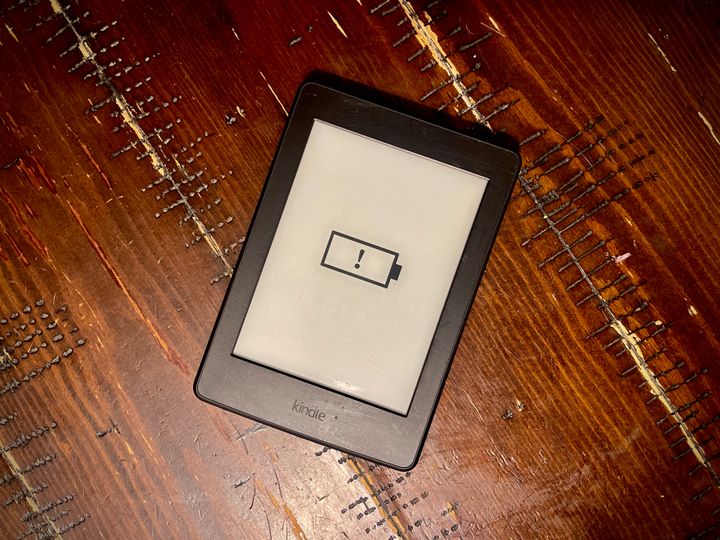 A kindle device sits on a table displaying an empty battery symbol.  