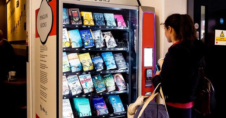 A person stands in front of a white and orange vending machine filled with books